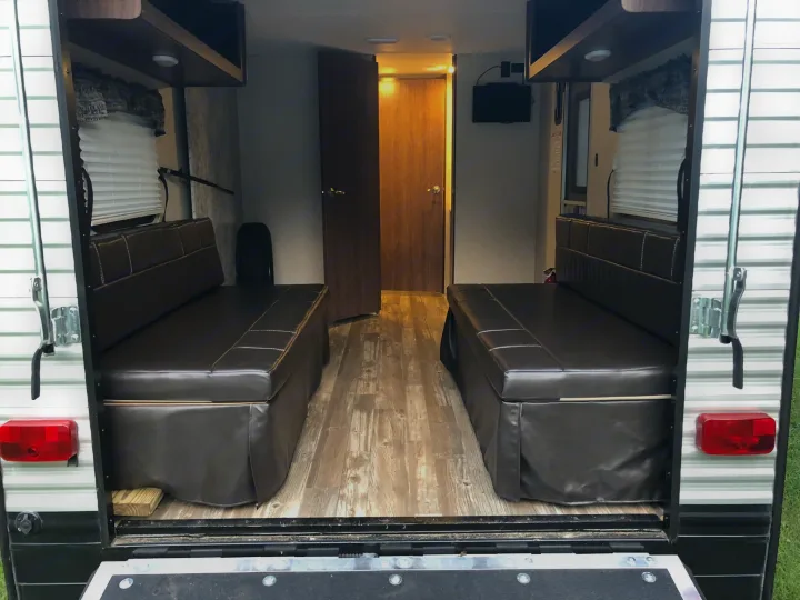 RV rental interior: view from the open rear ramp, showing two dark upholstered benches, wood-look floor, and doors ahead.. Heartland RVs Pioneer Toy Hauler 2017