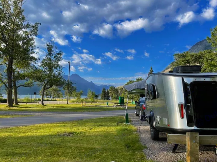 An RV rental trailer parked at a scenic lakeside campsite with mountains and trees, ideal for outdoor travel.. Airstream Basecamp 2022