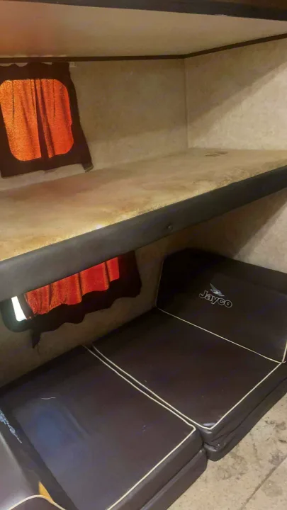 RV rental interior with comfortable bunk beds featuring brown cushions, curtains, and Jayco branding.. Jayco Jay Flight 2016