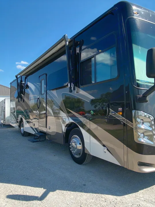 Stunning black and tan motorhome for rv rental, parked on gravel with an awning extended, under a bright blue sky.. Coachmen Sports Coach 339DS 2019