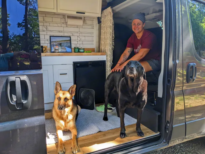 A happy woman pets her black Lab, while a German Shepherd rests in their spacious rv rental, with the door open to nature.. Dodge Ram 3500 Pro master 2022