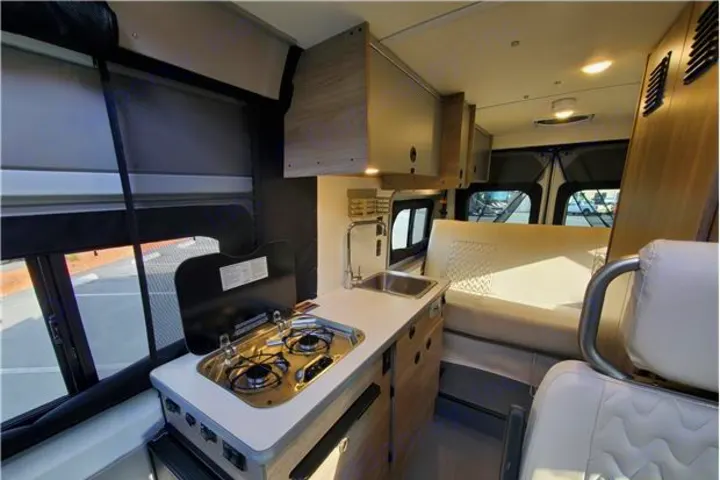 Clean RV rental interior: compact kitchen with stove & sink, plus cozy seating/bed area, perfect for travel.. Winnebago Solis 2022