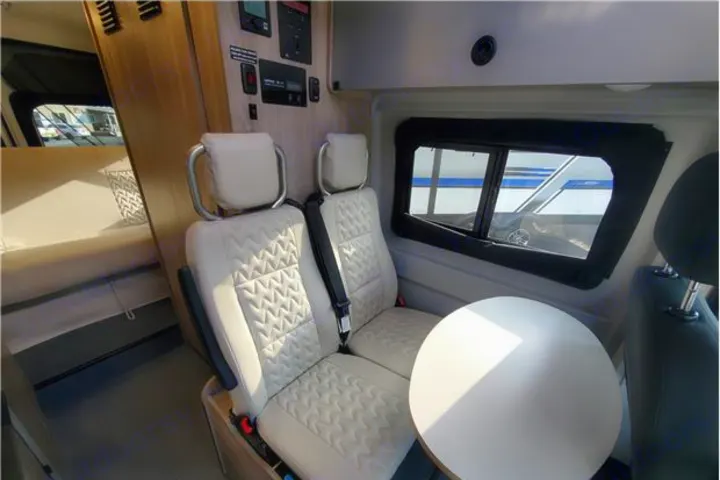 Experience an **RV rental**! Modern camper van interior features two quilted seats, a table, and a rear bed area.. Winnebago Solis 2022