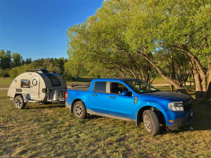 A blue Ford Maverick truck tows an RV rental teardrop trailer at a sunny campsite, ready for adventure.. Nucamp T@G 2022