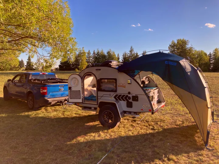 Blue Ford Maverick truck towing a T@G teardrop RV with awning extended. Perfect RV rental for camping trips.. Nucamp T@G 2022