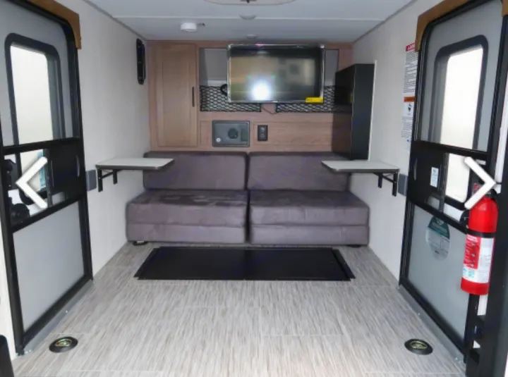 Bright RV rental interior featuring gray sofa seating, TV, and fold-down tables. Dual large doors for easy cargo loading.. Forest River NOBO 10.6 2022