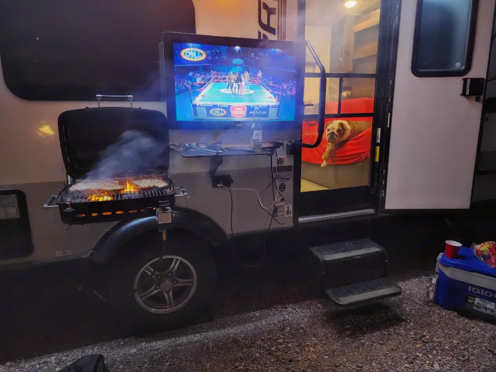An RV rental setup for a cozy night: grilling, TV with wrestling, and a bulldog peeking out from inside.. Forest River Rockwood Geo Pro 2018