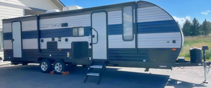 Grey Wolf travel trailer RV rental. This spacious recreational vehicle, with two doors and an extended awning, is parked outdoors.. Forest River Cherokee Grey Wolf 2021