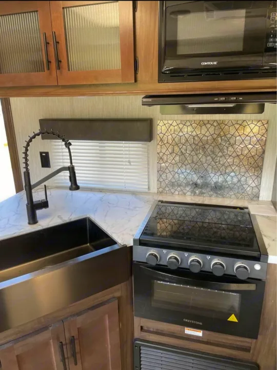RV rental kitchen: black farmhouse sink, modern stove & microwave, wood cabinets, and patterned backsplash create a stylish space.. Forest River Cherokee Grey Wolf 2021