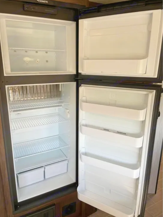 Clean, empty Dometic RV rental refrigerator with open doors. Top freezer, bottom fridge with shelves & bins.. Forest River Cherokee Grey Wolf 2021