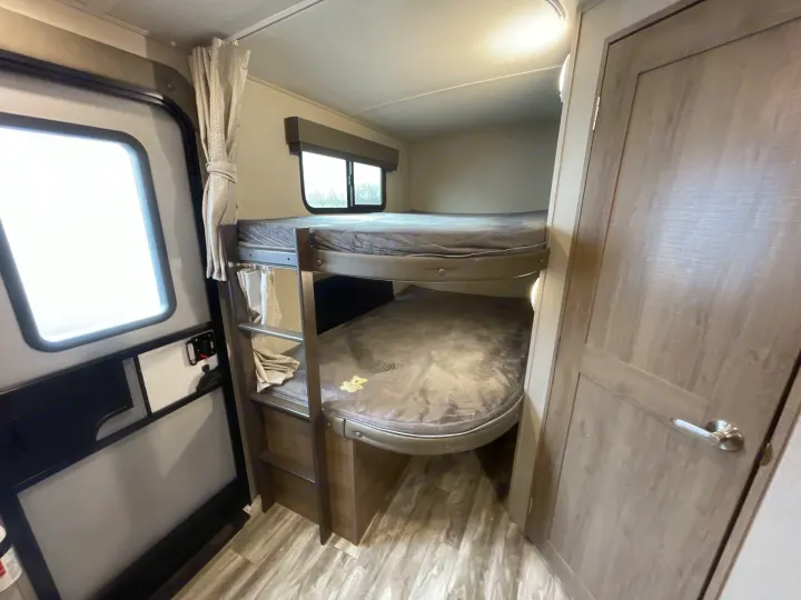 Experience comfort in this RV rental! Interior shows two bunk beds, complete with bedding and a ladder. Perfect for family adventures.. Grand Design Imagine 2400BH 2021