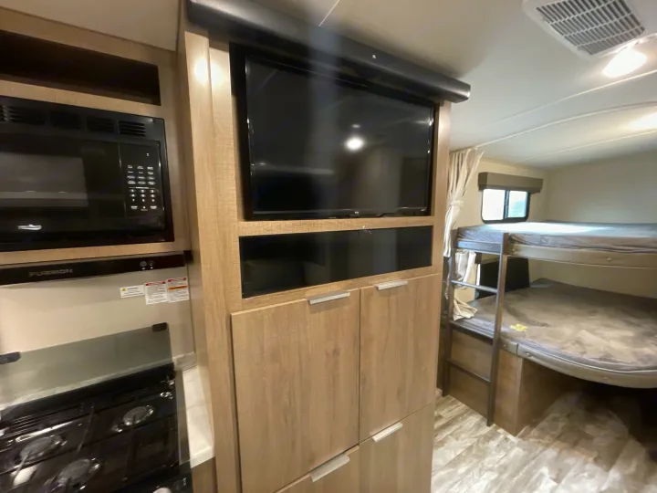 RV rental interior view: kitchen with microwave and stove, TV, and cozy bunk beds.. Grand Design Imagine 2400BH 2021