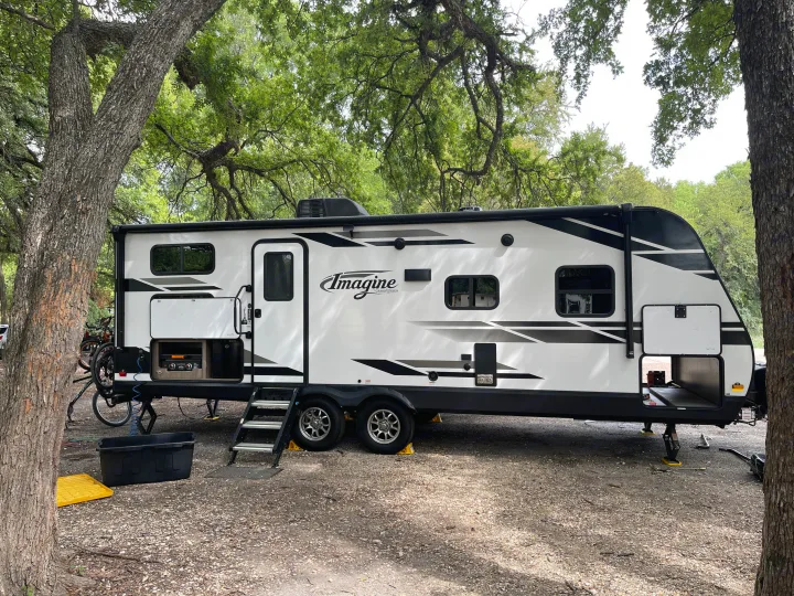 Imagine travel trailer rv rental parked at a serene, tree-shaded campsite with an outdoor kitchen and bikes.. Grand Design Imagine 2400BH 2021