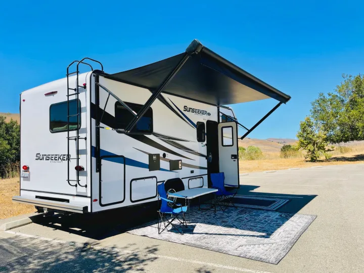 Bright Sunseeker RV rental ready for adventure: awning extended, with outdoor chairs & rug under a clear, sunny sky.. Forest River Sunseeker 2022
