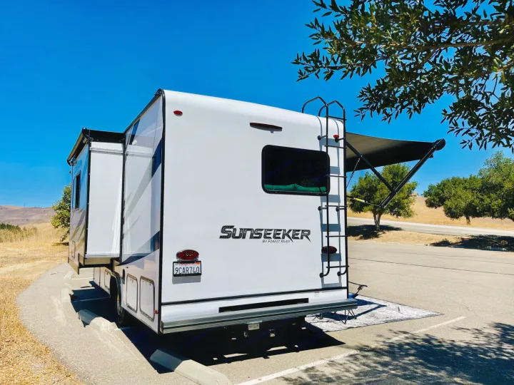 A white Forest River Sunseeker RV rental is parked, awning extended, amidst sunny, dry hills.. Forest River Sunseeker 2022