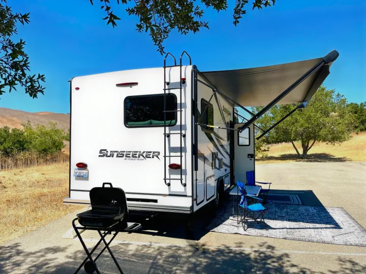 Sunny RV rental campsite: a white Sunseeker motorhome with an extended awning, outdoor seating, and grill ready for fun.. Forest River Sunseeker 2022