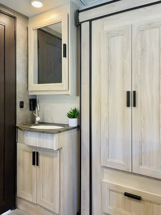 Modern RV rental: light wood bathroom vanity, sink, mirror, and built-in storage with black pulls.. Forest River Sunseeker 2022