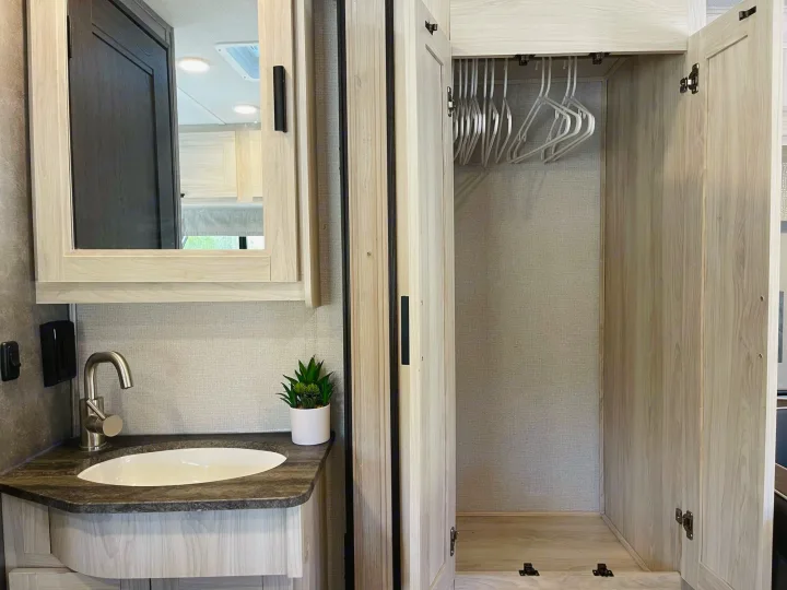 Spacious RV rental interior featuring a modern vanity with sink and mirror, plus an open closet with hangers.. Forest River Sunseeker 2022