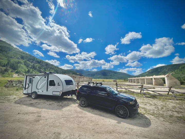 Perfect RV rental setup: Black SUV and travel trailer parked in a scenic mountain setting, with historic ruins nearby.. R-Pod Hood River Edition 2020