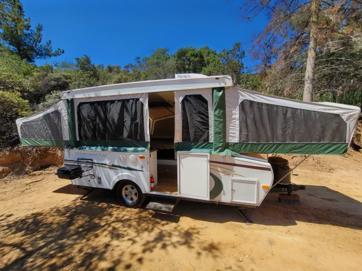 This RV rental pop-up camper is set up for camping in a sunny, tree-lined outdoor campsite, perfect for adventure.. Starcraft Centennial 2005
