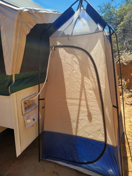 An RV rental's outdoor shower setup: a beige privacy tent connected to the camper, with hose and spigots visible for camping.. Starcraft Centennial 2005