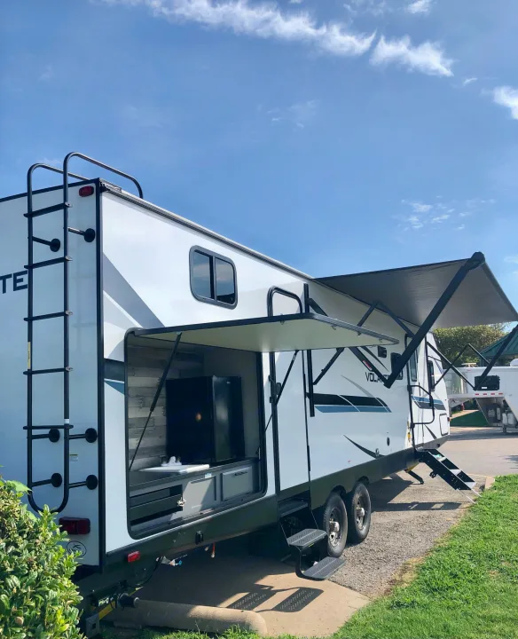This **RV rental** features an open outdoor kitchen and extended awning, perfect for camping under a bright blue sky.. Crossroads RV Volante 2022