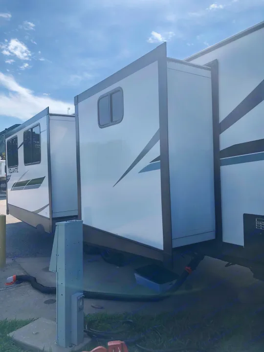An RV rental at a campground. Its slide-outs are extended, revealing more interior space and utility hookups below.. Crossroads RV Volante 2022