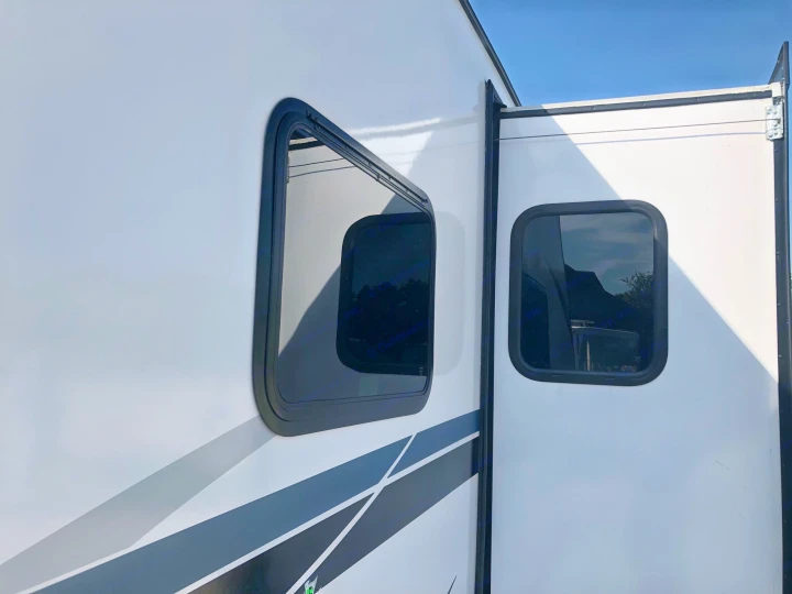 Side view of a white RV rental with an extended slide-out section, featuring two dark-tinted windows. Ready for your next adventure.. Crossroads RV Volante 2022