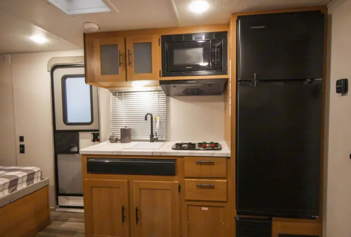 This RV rental kitchen boasts a sink, stovetop, microwave, and fridge, ideal for camping adventures.. Forest River Avenger 2022