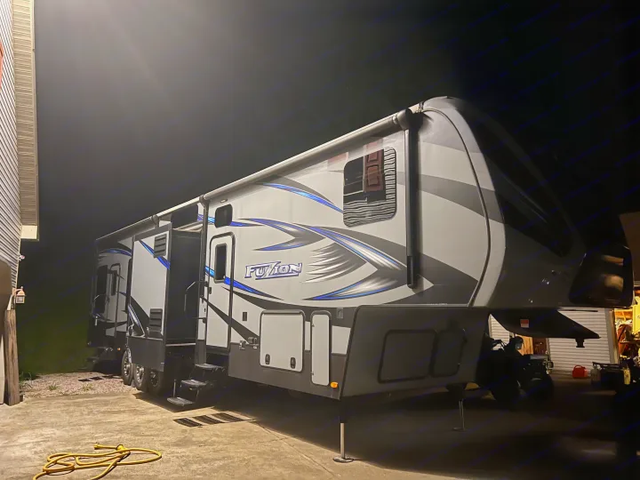A large, sleek Fuzion toy hauler RV, brightly lit at night. Consider this for your next rv rental or camping trip!. Keystone Fuzion 2015