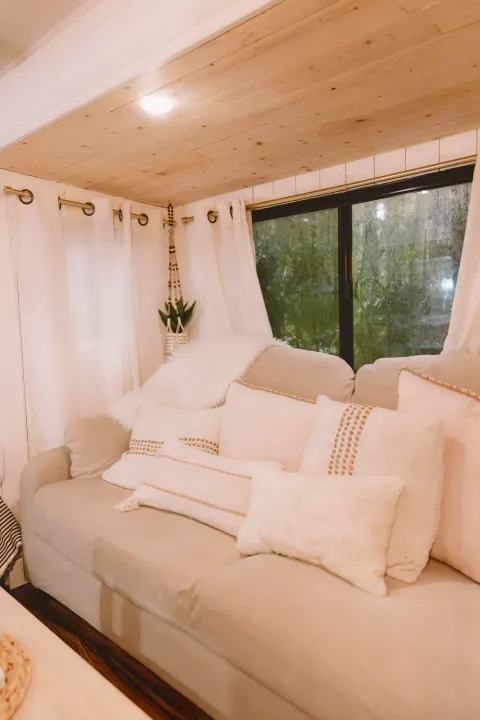 Relax in this inviting RV rental. Plush sofa with decorative pillows, wood ceiling, white curtains, and a window with a rainy view.. Forest River Other 2013