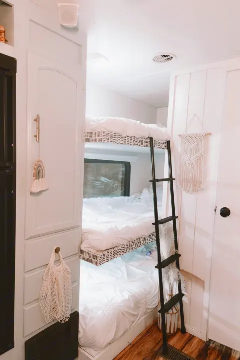 Inside a bright RV rental: three cozy bunks with white bedding, a black ladder, and wood floors. Ideal for family adventures.. Forest River Other 2013
