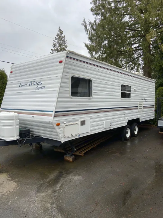 White "Four Winds Express" travel trailer parked outdoors on a wet surface. Perfect for your next rv rental adventure!. Dutchmen Express 2001