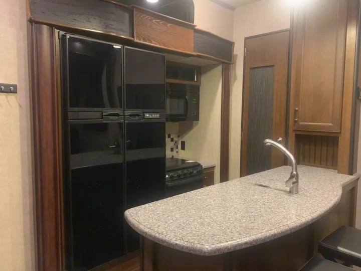 Well-equipped RV rental kitchen: large black fridge, microwave, stove, and a granite-look curved counter with sink.. Keystone Fuzion 2015