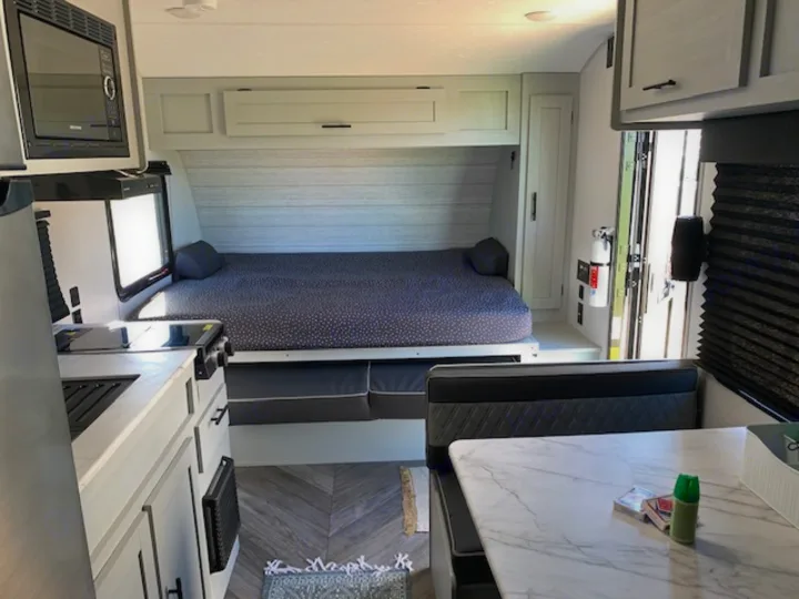Inside a modern RV rental: compact kitchen with microwave, large bed, and dinette seating. Light wood floors and grey cabinets throughout.. Forest River Salem FSX 2022