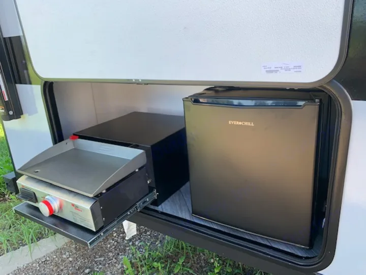 An RV rental's outdoor kitchen features a pull-out griddle and a black Everchill mini-fridge, ready for your camping trip.. Forest River Salem FSX 2022