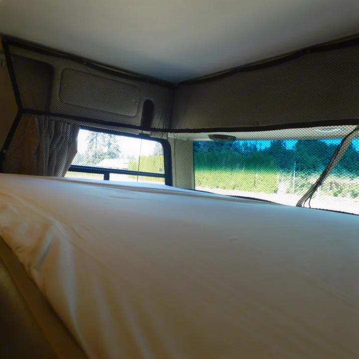 RV rental overhead bunk bed with safety net and bright outdoor view. This cozy sleeping area is ready for adventure.. Coachmen Pursuit 2017