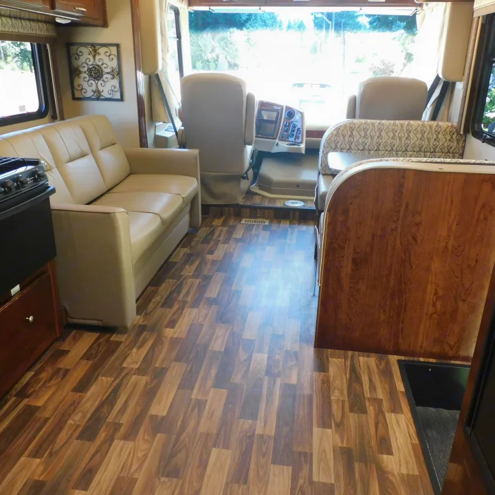 Spacious RV rental interior with light-colored sofa, dining booth, and wood-look flooring. Bright and inviting for travel.. Coachmen Pursuit 2017