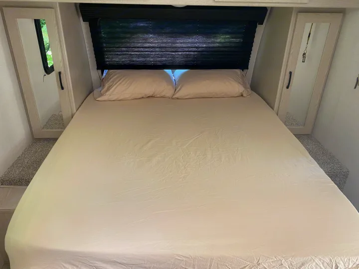 Comfortable RV rental bedroom featuring a clean bed, overhead blind, and mirrored closets.. Coachmen Apex 2021