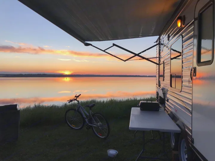 Lakeside RV rental enjoys a vibrant sunset. Travel trailer with an awning, bike, and grill setup on the grass.. Jayco Jay Flight SLX 2017