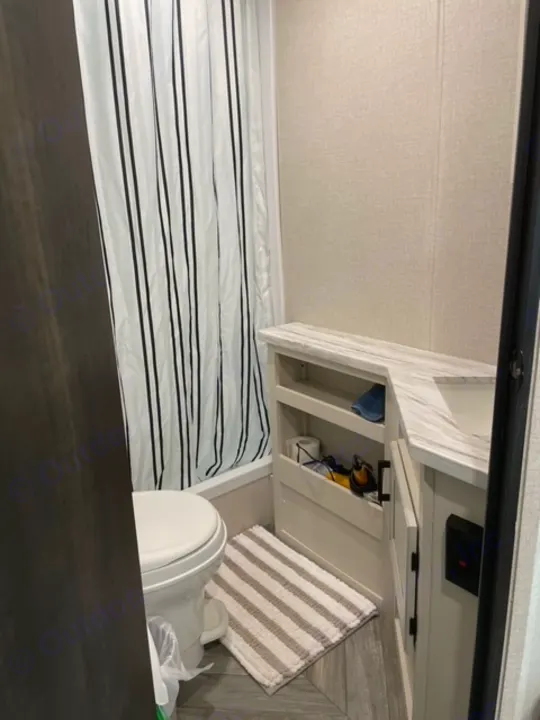 A compact RV rental interior features a striped bed, a toilet, and accessible storage cubbies, maximizing space.. Highland Ridge RV Olympia 2022