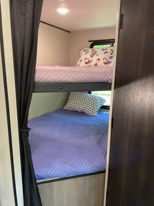 Two cozy bunk beds inside an RV rental, featuring soft pink and blue quilted bedding and decorative pillows.. Highland Ridge RV Olympia 2022