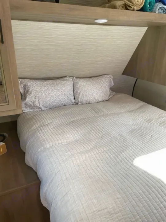 Cozy RV rental bedroom featuring a neatly made bed with pillows, alongside compact built-in storage.. Highland Ridge RV Olympia 2022