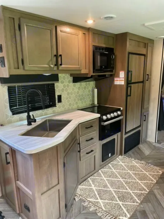 Modern RV rental kitchen with refrigerator, microwave, stove, sink, and ample storage for comfortable travel.. Highland Ridge RV Olympia 2022