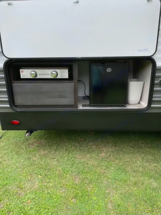 RV rental showing its outdoor kitchen: a mini-fridge, Blackstone griddle, and counter built into the side, on grass.. Highland Ridge RV Olympia 2022