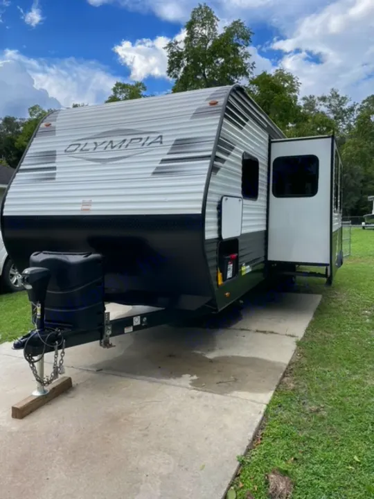 White & black Olympia travel trailer, a great RV rental option parked on concrete under blue skies.. Highland Ridge RV Olympia 2022