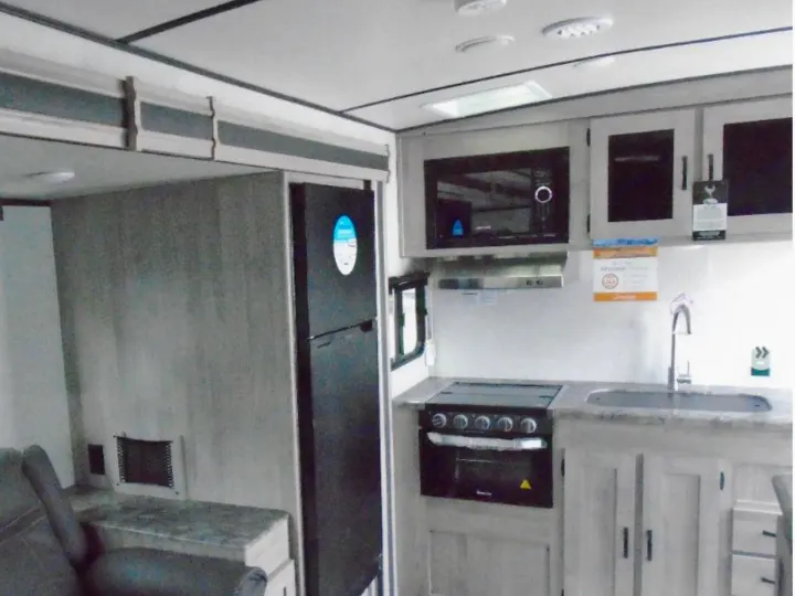 Modern RV rental interior with compact kitchen appliances: microwave, stove, fridge, and sink. Visible seating adds to the living space.. Other Other 2022