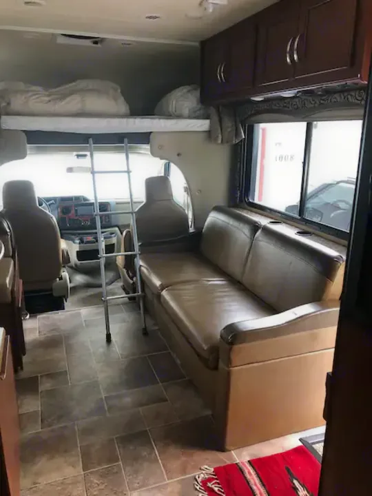 Bright rv rental interior featuring a front cab, overhead bunk, and beige sofa.. Thor Four Winds 2017