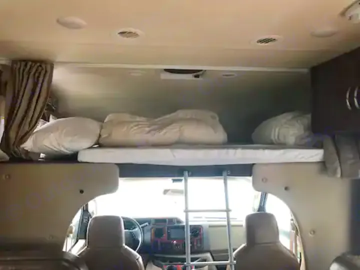 Spacious RV rental interior showing an overhead sleeping bunk with bedding and ladder leading to the front cockpit.. Thor Four Winds 2017