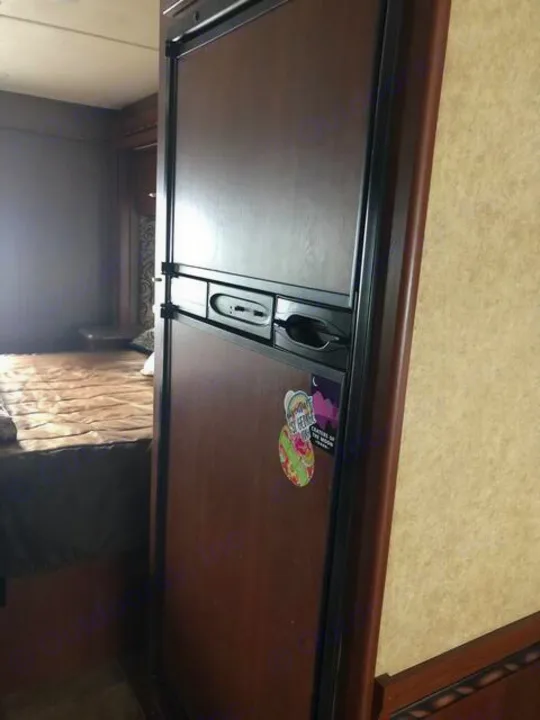 View inside an RV rental: a wood-paneled refrigerator, with the compact bedroom visible to the left.. Thor Four Winds 2017